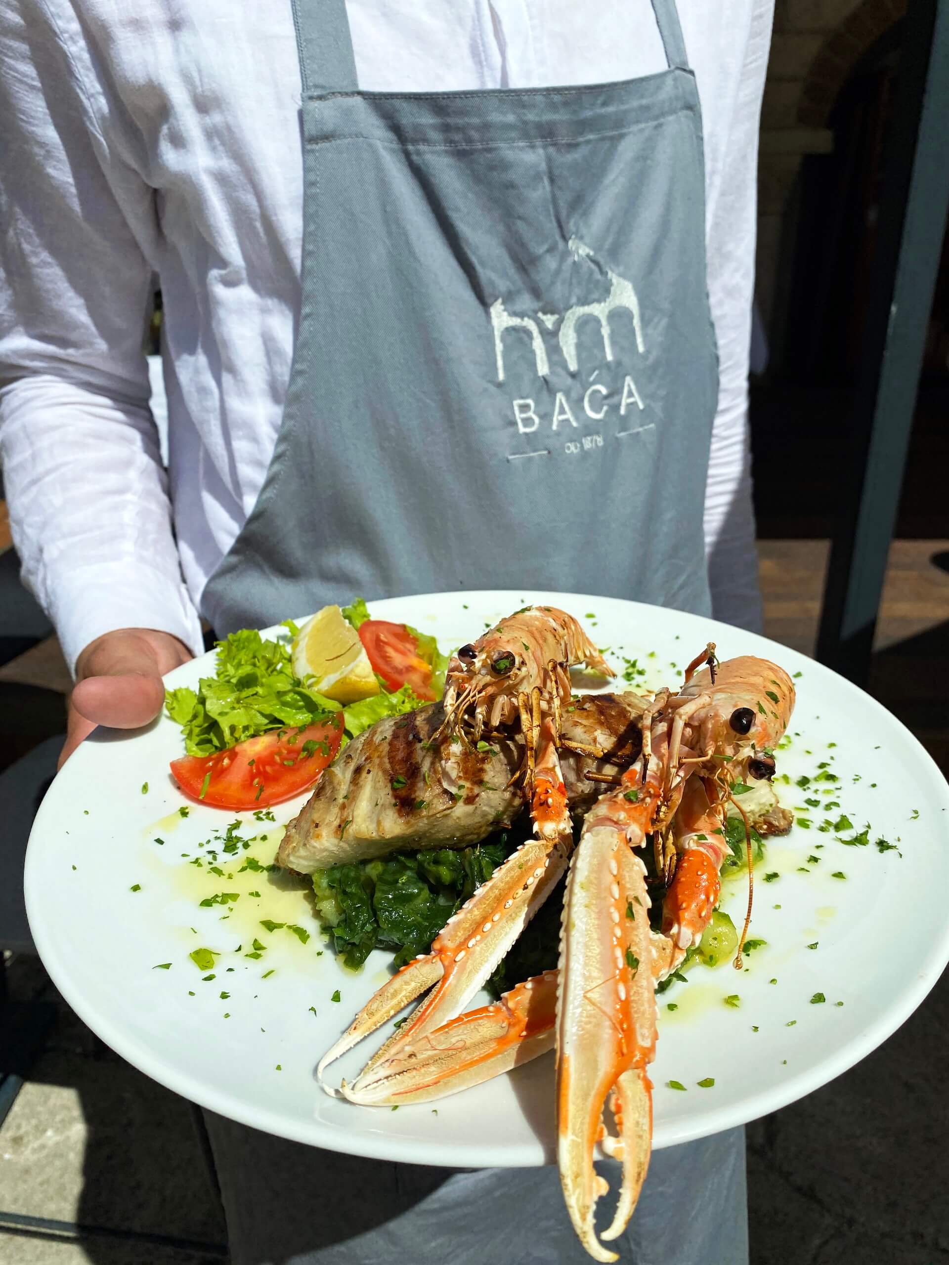 A waiter holding a plate of grilled langoustines and fish steak.