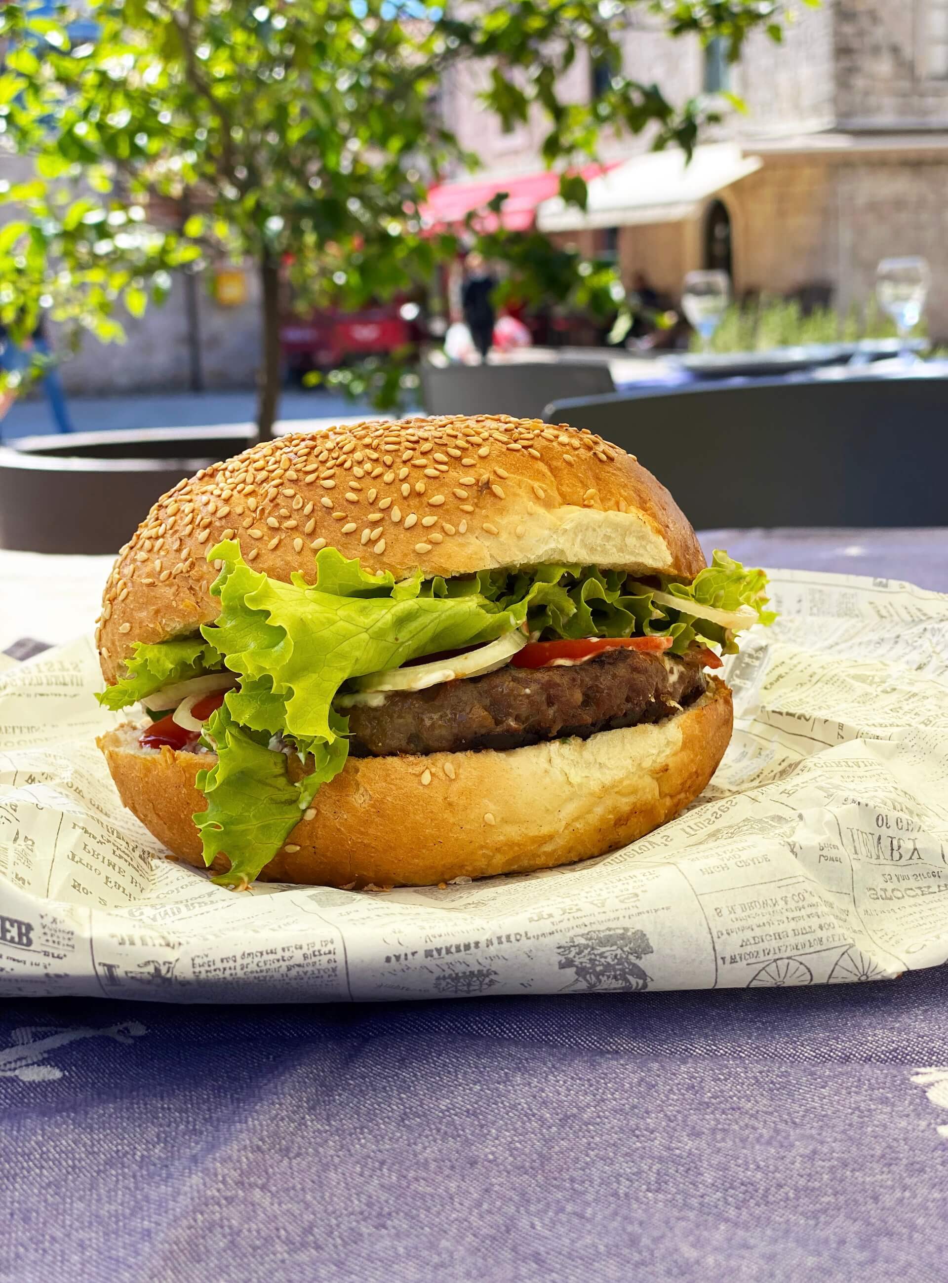 The Baća burger on a sesame bun, wrapped in newsprint paper.