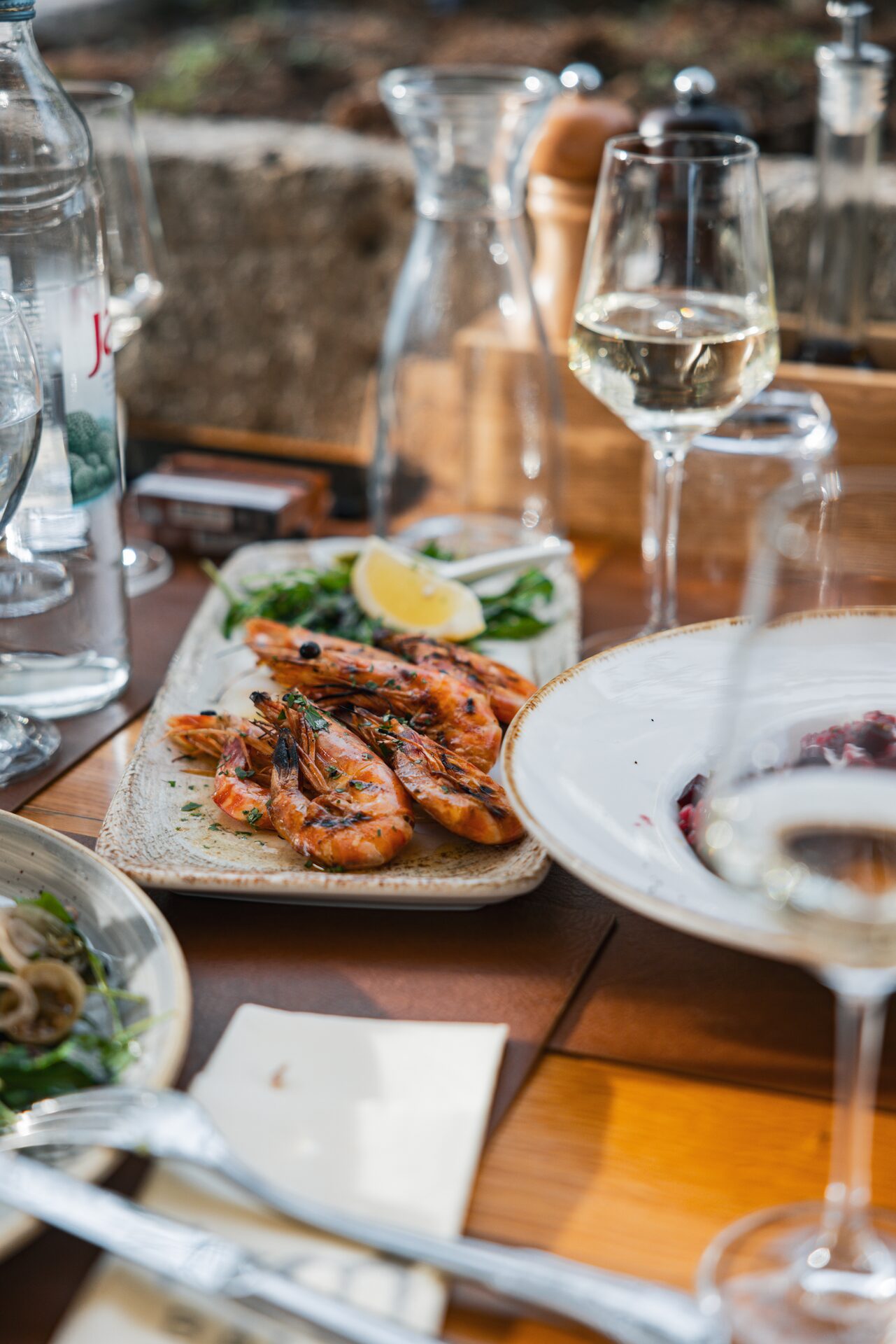 Grilled prawns and glasses of white wine on a freshly set table.