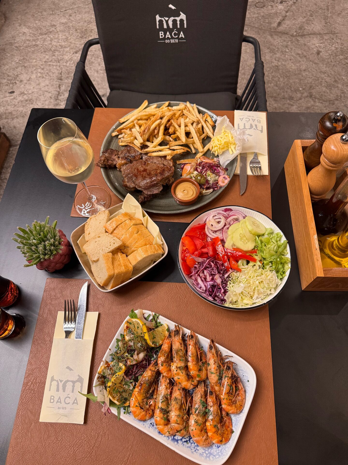 A table for two: grilled steak with fries, grilled prawns, a mixed salad, bread and a glass of white wine.