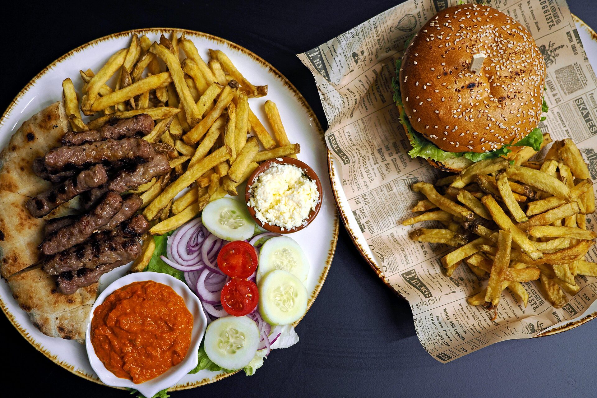 Ćevapi with flatbread, ajvar and fresh vegetables, next to the Baća burger with fries.