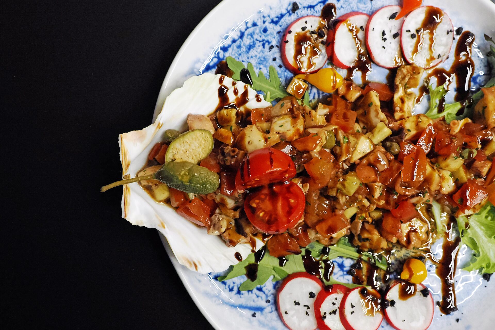 Octopus salad with tomatoes, capers and radish, served in a scallop shell.